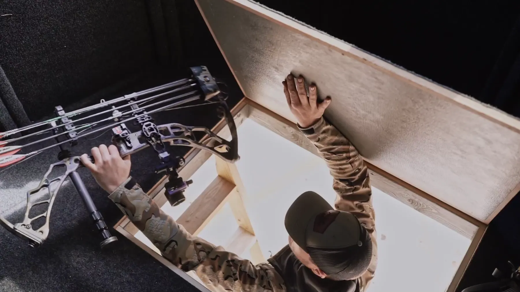 A hunter passing a bow up through the floor hatch of a NXTGen blind.