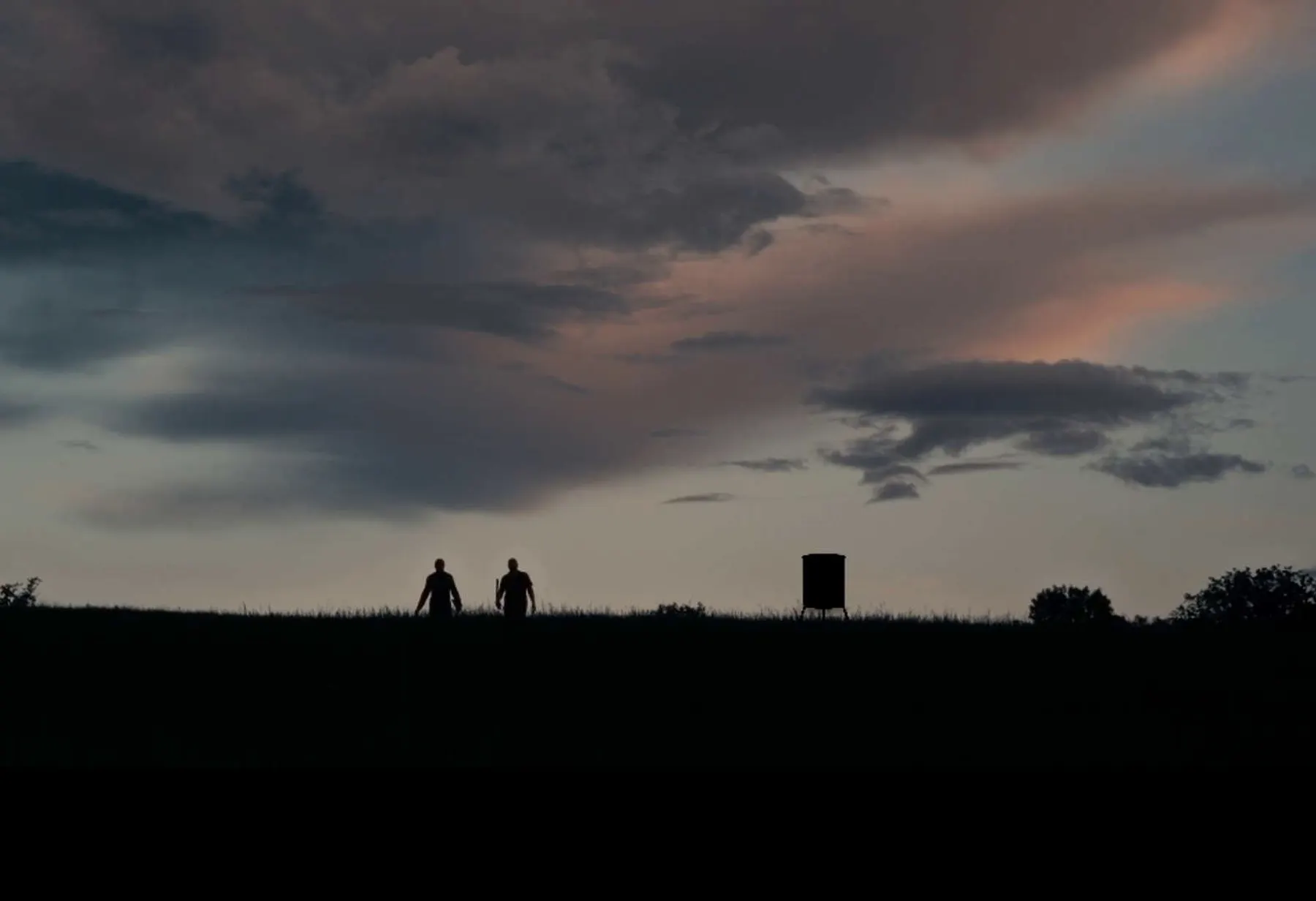 Two people walking a ridge at last light with a blind on the skyline.